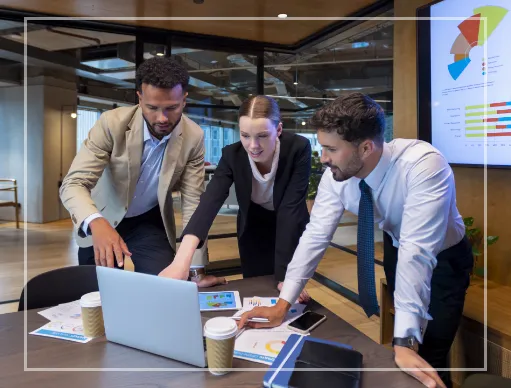 2 men and 1 women standing at a table all pointing at a laptop screen. 